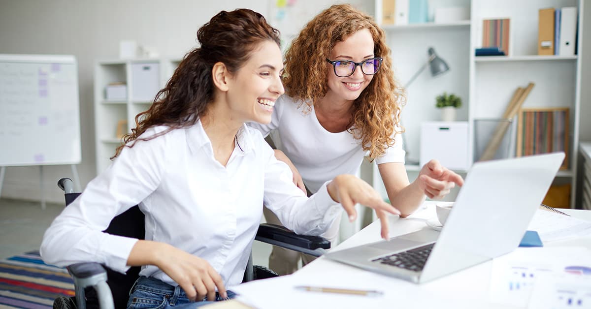 Two people, one using a wheelchair, are looking at a laptop.