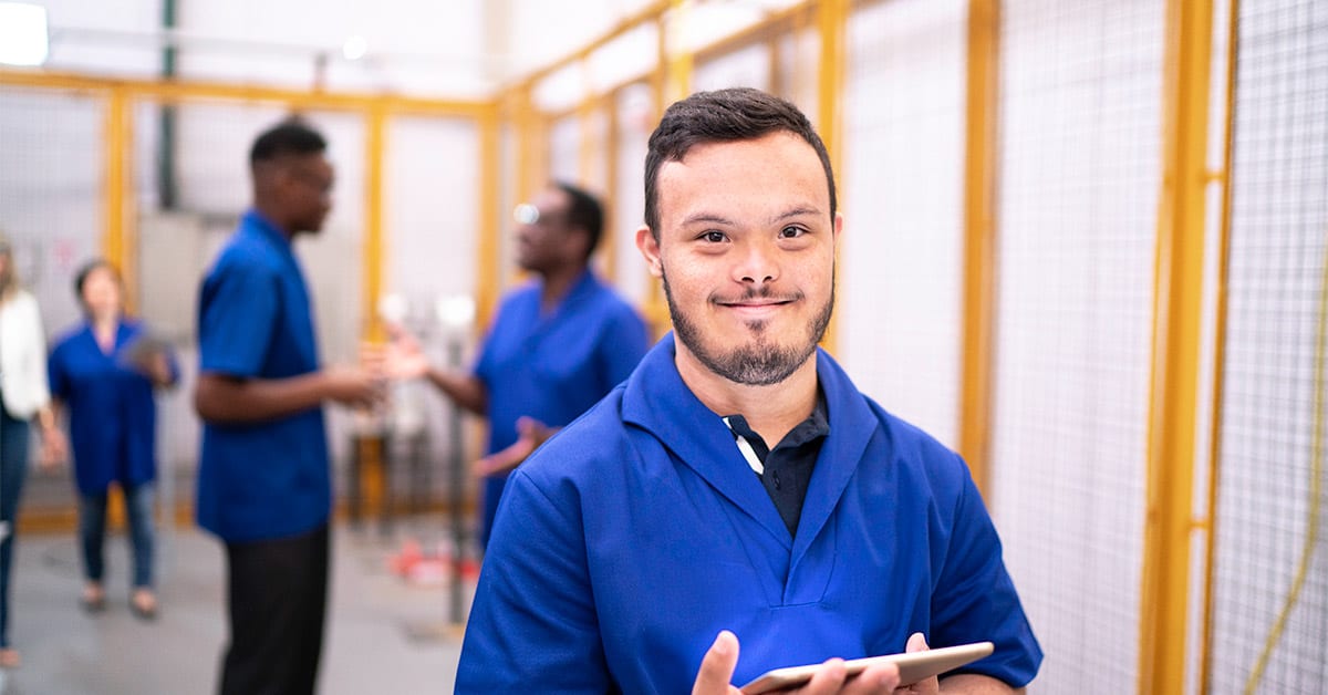 A worker with Down syndrome walks in a hallway with other workers in the background.