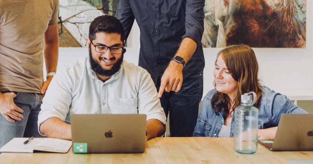 4 people looking at one laptop screen on a desk