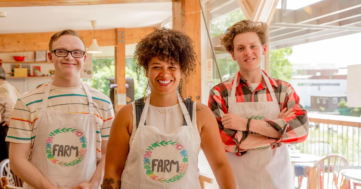 Three individuals wearing aprons standing in a store smile at the camera.