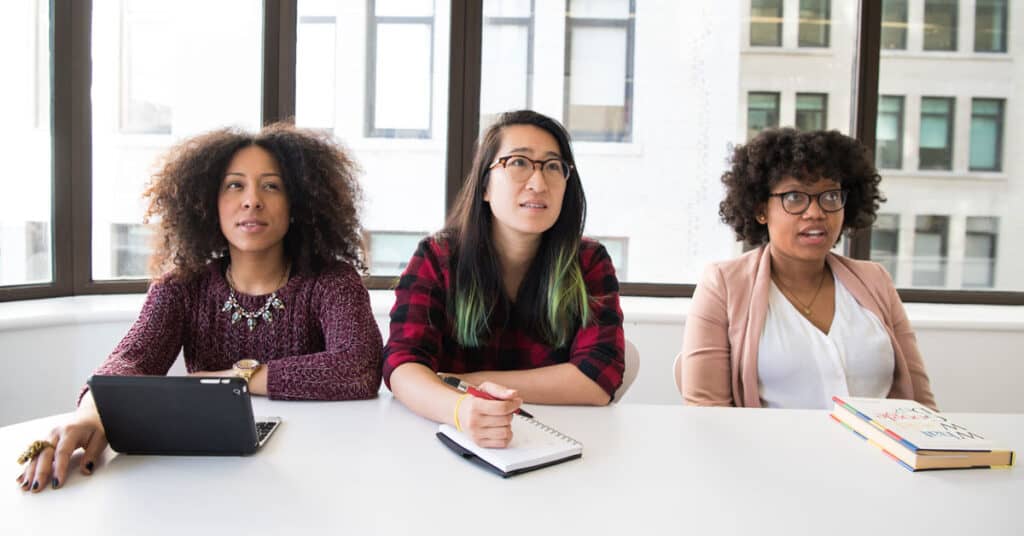 trois personnes à une table de réunion, deux à la peau moyennement foncée et une à la peau claire-foncée