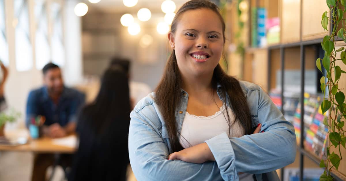 A woman in a jean jacket smiling and crossing her arms.