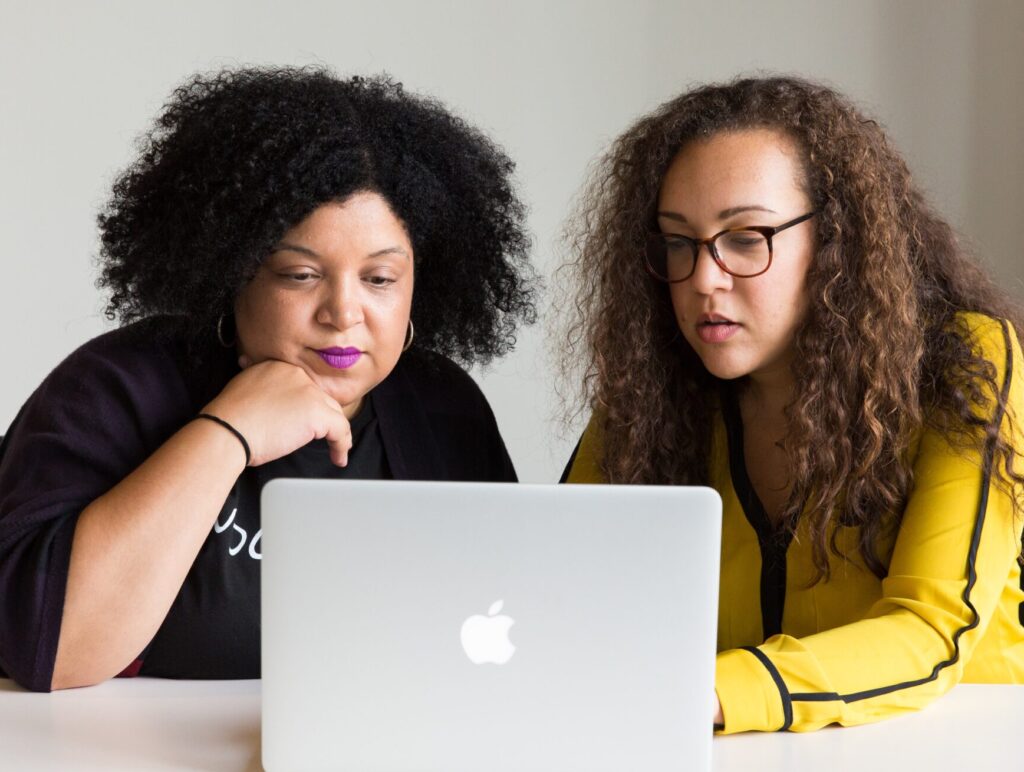 Two people sit beside each other looking at a laptop.