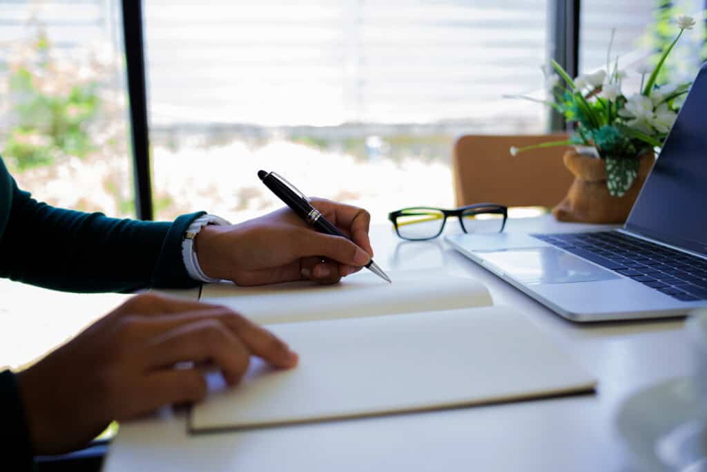 Une personne est assise à un bureau près d'une fenêtre dans un bureau, écrivant dans un cahier avec un ordinateur portable devant elle. Les cours CASE permettent aux employeurs de s'engager dans un développement professionnel continu lorsque cela correspond le mieux à leur emploi du temps.