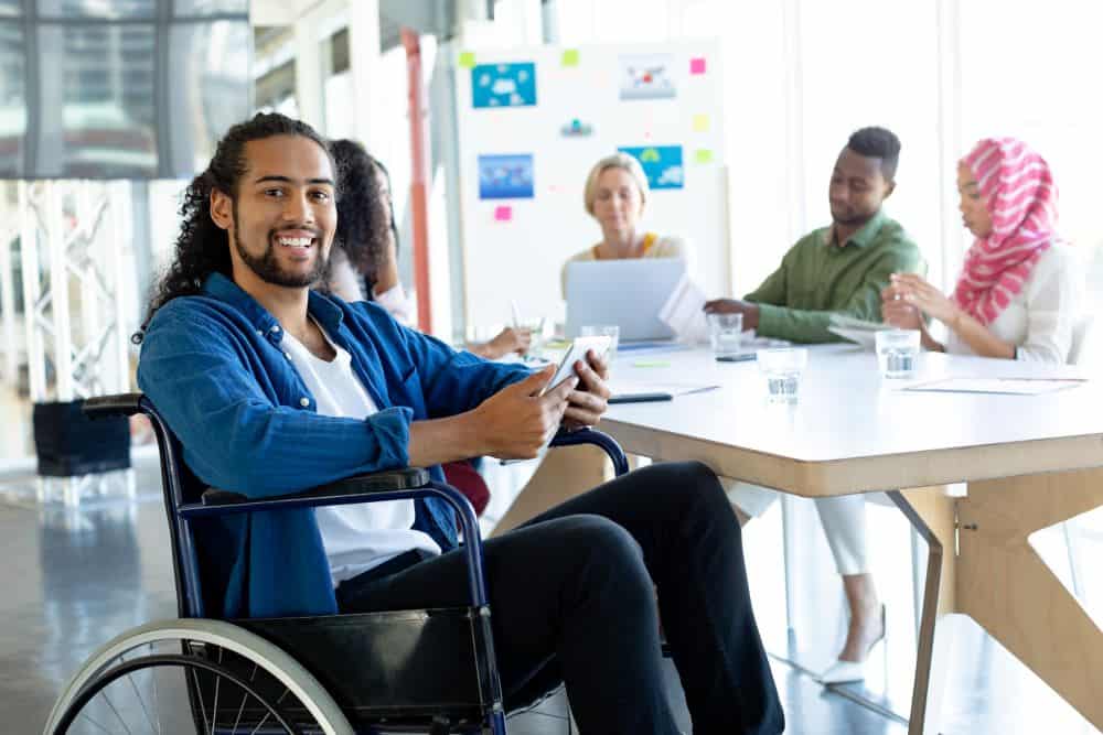 Une personne noire en fauteuil roulant travaille à une table avec des collègues.