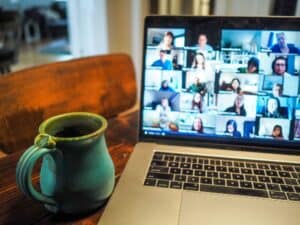 A mug is beside a laptop in someone's home. Faces fill the laptop screen.