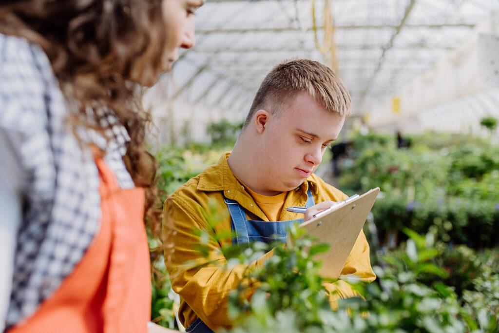 An experienced woman florist helping young employee with Down syndrome in garden centre.