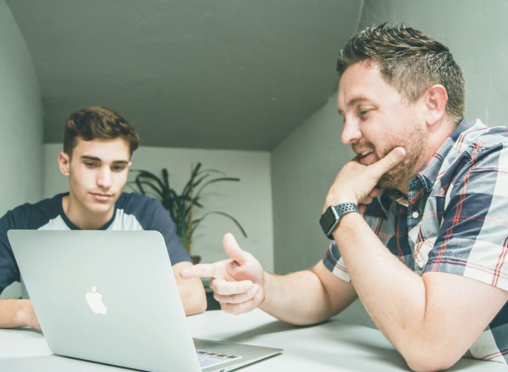 A supervisor speaks with a young worker while showing them a laptop.