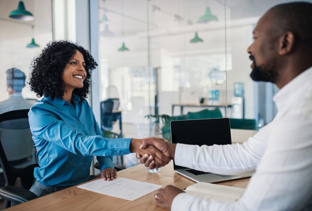 Two people shaking hands in a meeting room. The image represents the value of effective marketing for career practitioners in connecting with employers and creating opportunities for clients.