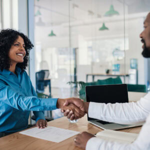 Two people shaking hands in a meeting room. The image represents the value of effective marketing for career practitioners in connecting with employers and creating opportunities for clients.