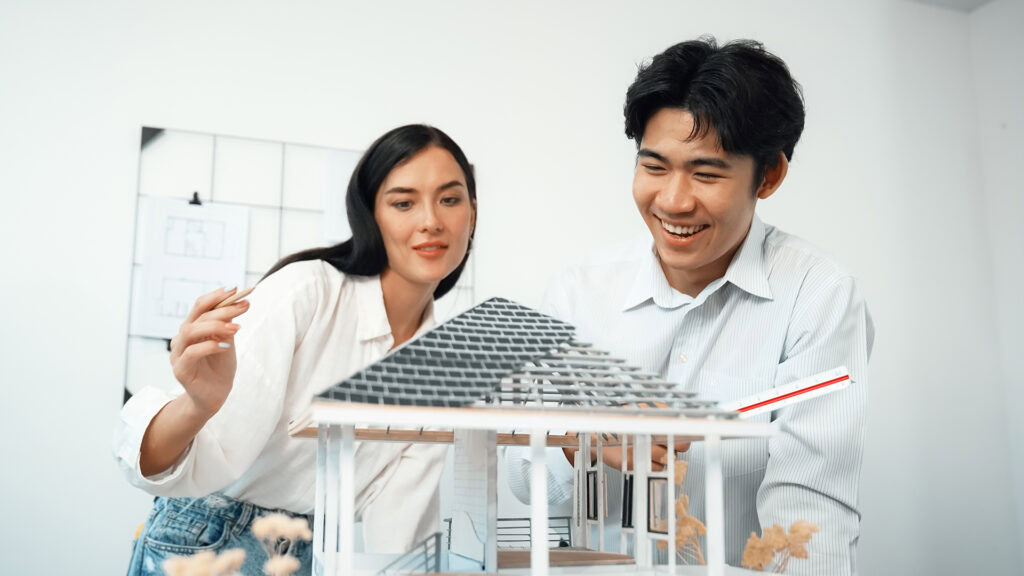 Two architects smiling while working together on a three-dimensional model design for a house. The image represents the value of working in strengths-based careers that align with our skills and passions.