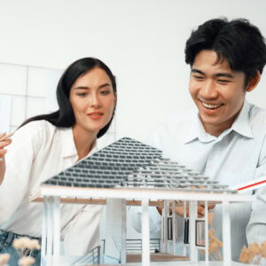 Two architects smiling while working together on a three-dimensional model design for a house. The image represents the value of working in strengths-based careers that align with our skills and passions.