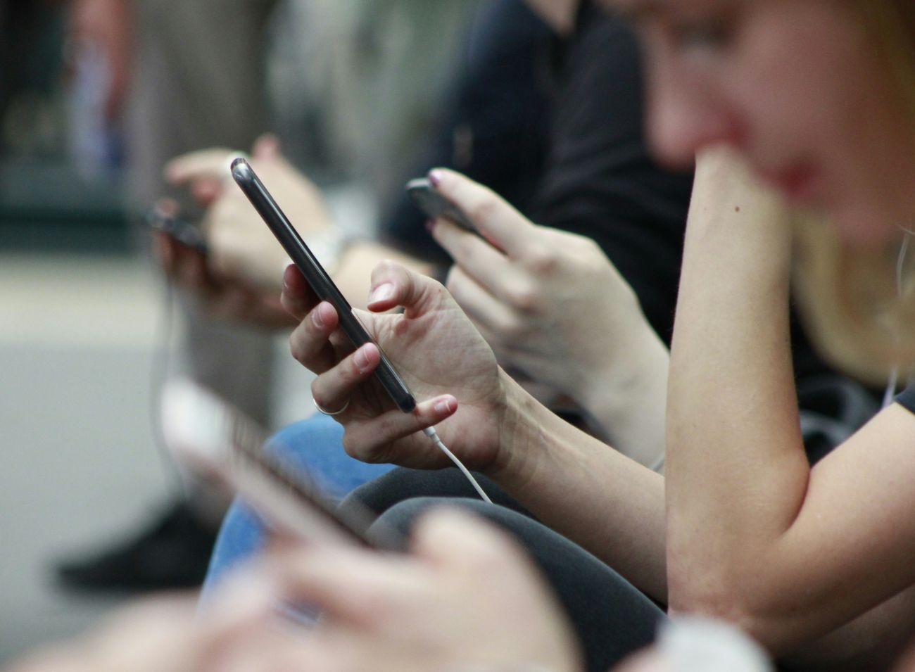 Various people sitting side-by-side and looking at their cell phones.