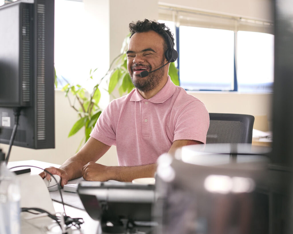 A person experiencing disability using a headset and working on a computer at a call centre.