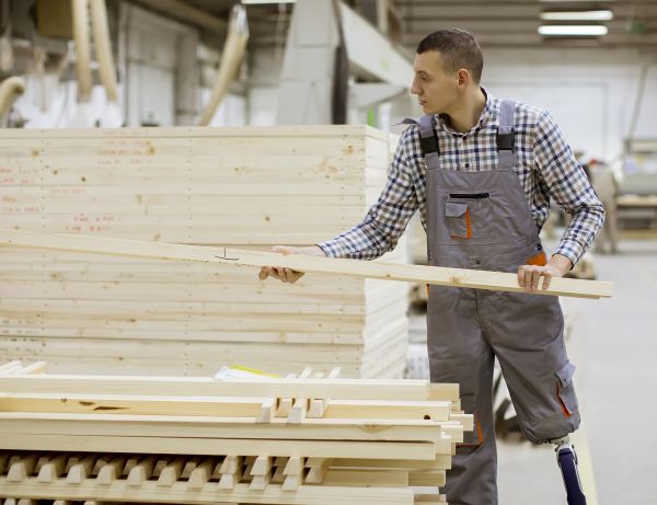 A person with an artificial limb below the left knee picks up a 2x4 in a shop.