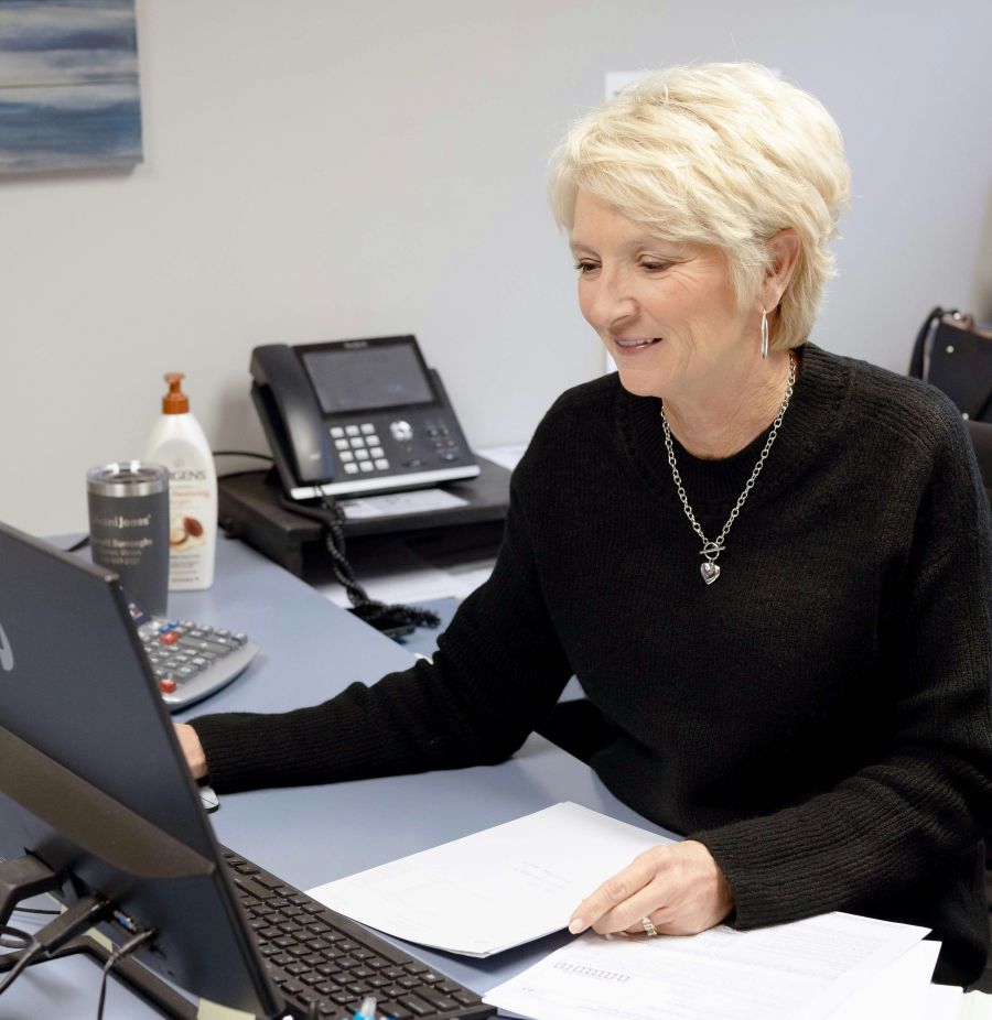 Mature worker sitting at a desk with papers on it and looking at a monitor.