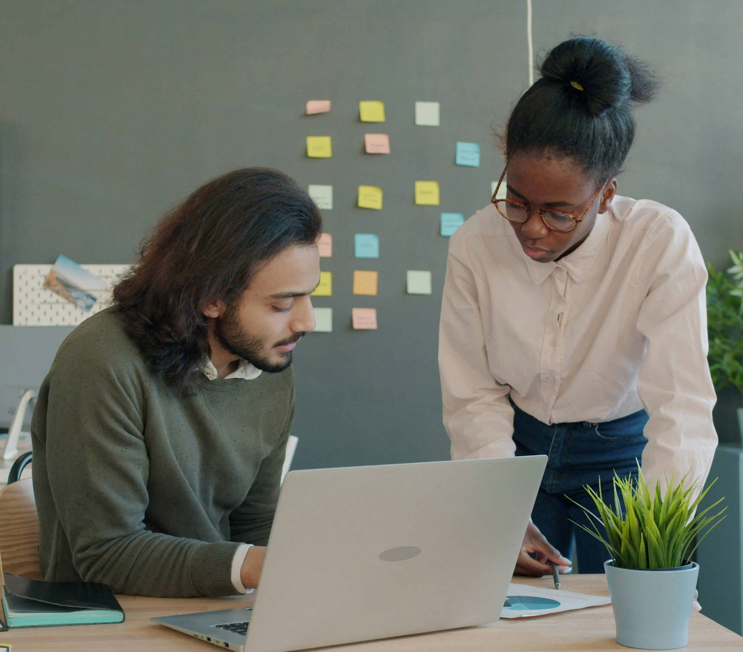 An employment service provider is standing beside a client who is sitting at a table with a laptop.