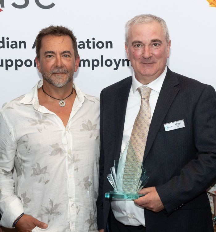 Photo of Garth Johnson and Jeff Foster, the latter of which is holding an award made of clear glass with a green tinge.