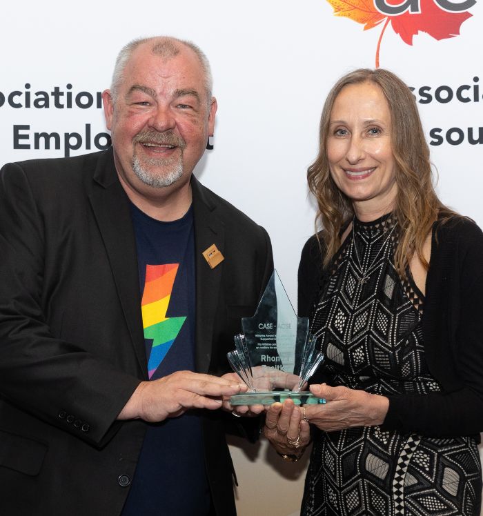 Photo of Sean Wiltshire and Rhonda Zasitko, who is holding an award made of clear glass with a green tinge.