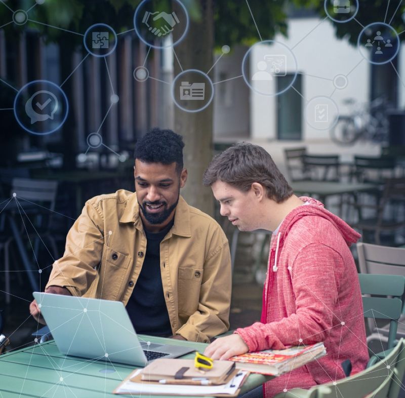 A mentor and mentee sit at a table and look at a laptop screen. Multiple light blue circles with different icons are connected with lines and overlay the top of the photo.