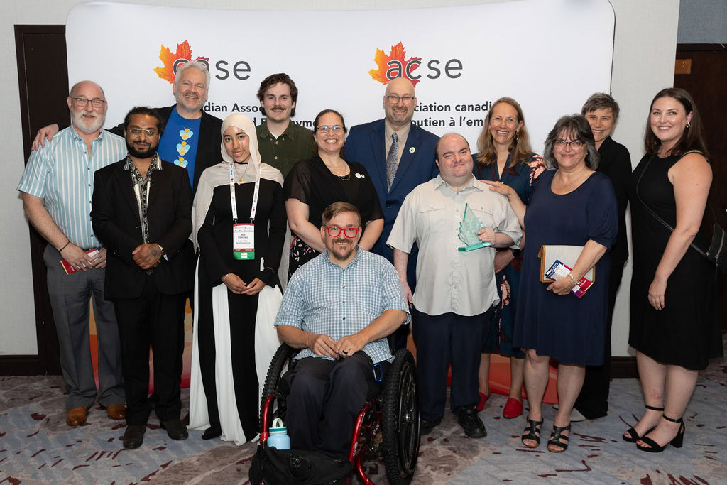 Group of people stand in front of a banner for the Canadian Association for Supported Employment