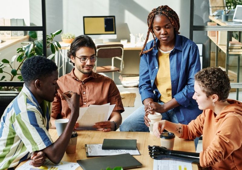 Four diverse people are talking while sitting at a table at work.