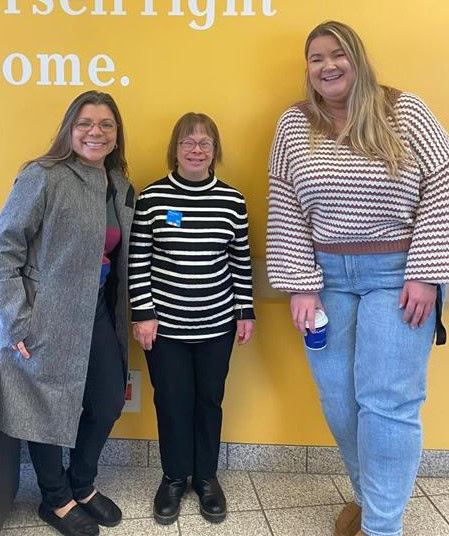 Three people smiling and standing in front of a bright yellow wall.