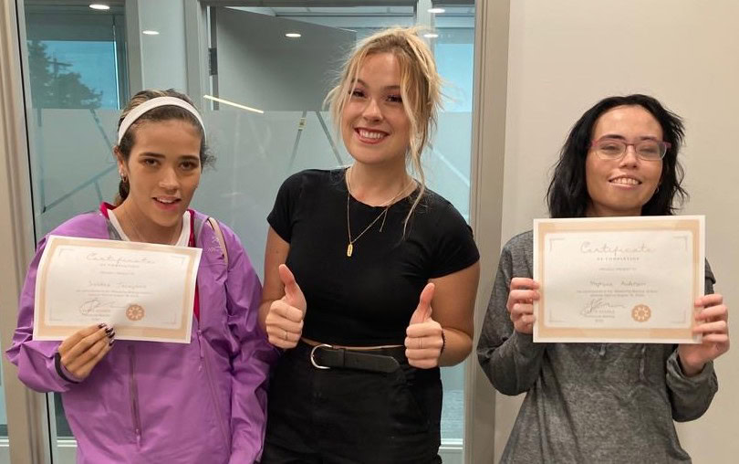 Three people are standing and smiling, with the two on either side holding a certificate.
