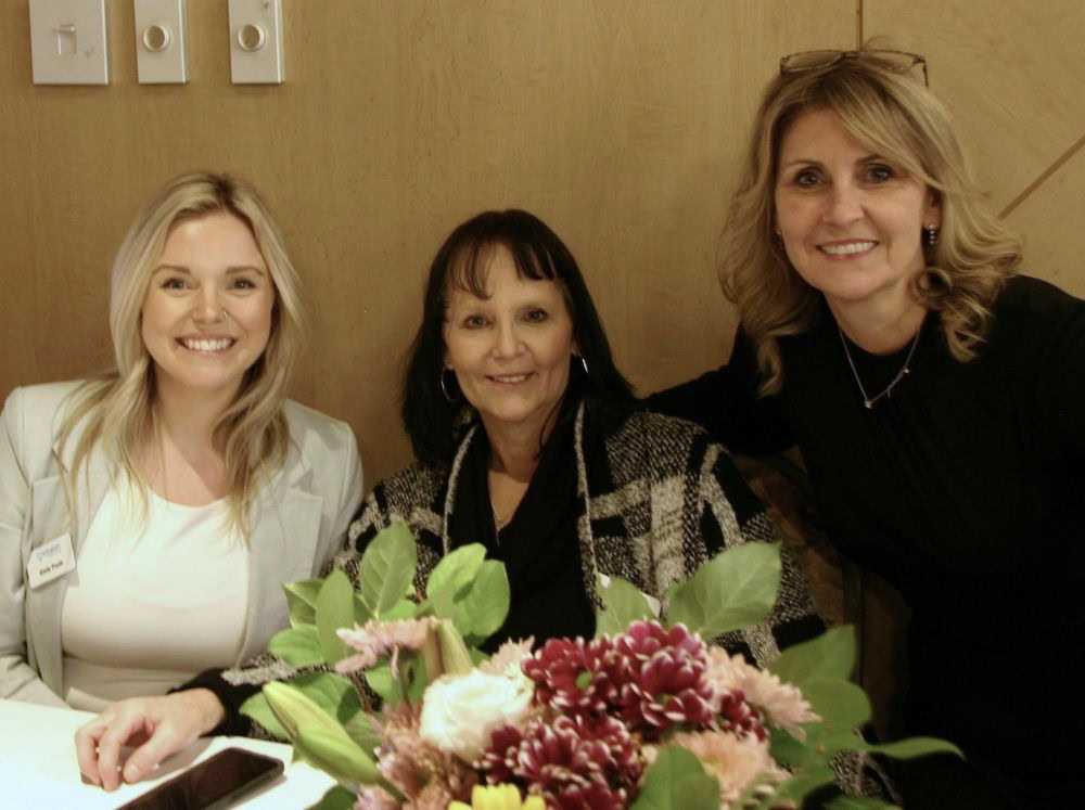 Three people smile at the camera, with a bouquet in front of them.