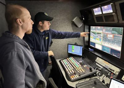 Two people look at monitors in a broadcasting booth.
