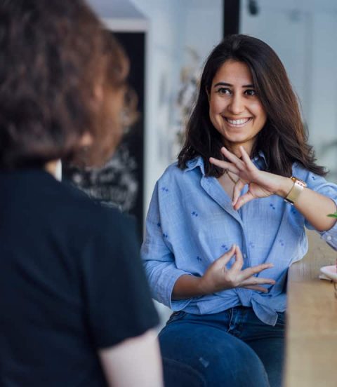 A woman in blue signing to another woman in a black shirt