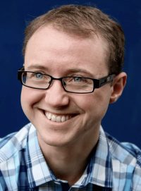 Mick Schubert. Light-skinned man with short brown hair and blue eyes wearing black glasses and smiling.