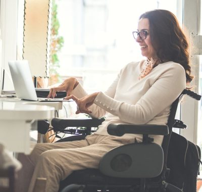 Person who uses a wheelchair is working on a laptop.
