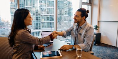 Happy Hispanic job candidate shaking hands with Asian businesswoman after successful interview in the office.